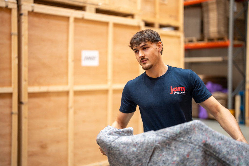 Jam Storage team member carrying a wrapped armchair into a storage container
